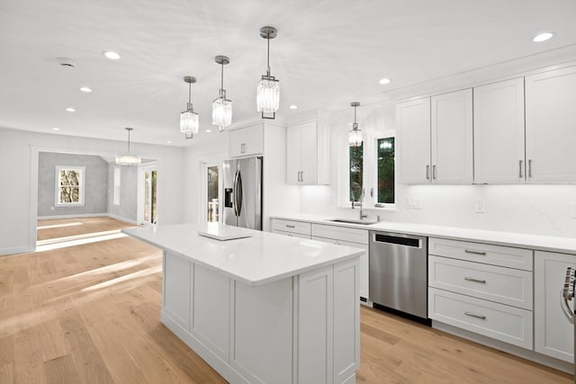 kitchen featuring decorative light fixtures, stainless steel appliances, a kitchen island, and light hardwood / wood-style floors