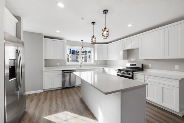 kitchen featuring appliances with stainless steel finishes, a kitchen island, pendant lighting, hardwood / wood-style floors, and white cabinetry