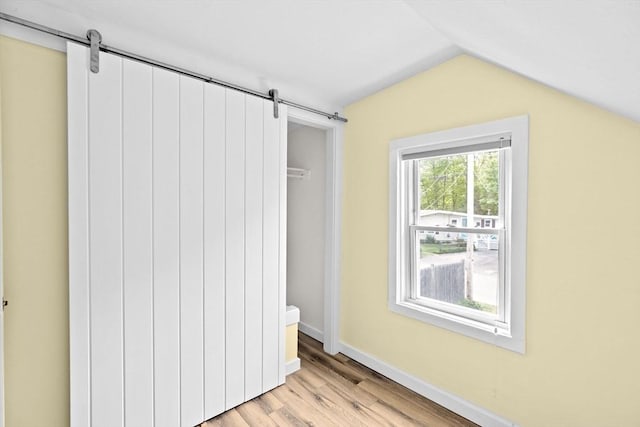 216 Waltham St, Hanson, MA 02341 - unfurnished bedroom featuring a barn door, vaulted ceiling, light wood-style floors, and baseboards
