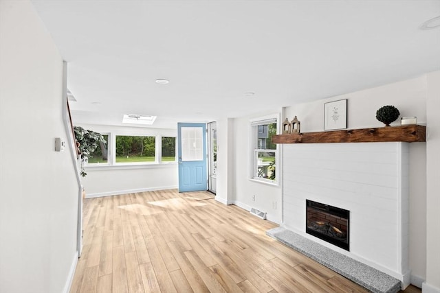 216 Waltham St, Hanson, MA 02341 - unfurnished living room with a fireplace with raised hearth, baseboards, light wood finished floors, and a skylight