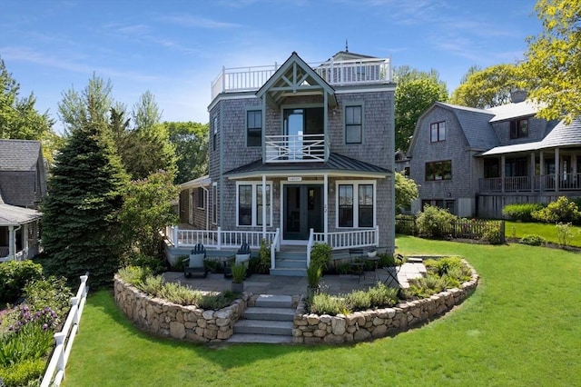 view of front facade with a balcony, covered porch, a front lawn, and a patio