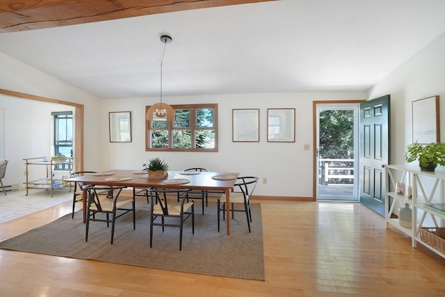 dining area with baseboards, vaulted ceiling, and light wood-style floors