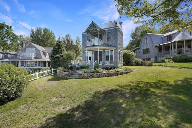 rear view of property featuring a balcony, fence, a porch, and a yard