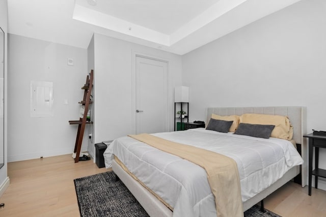 bedroom featuring electric panel, light wood-type flooring, and a raised ceiling