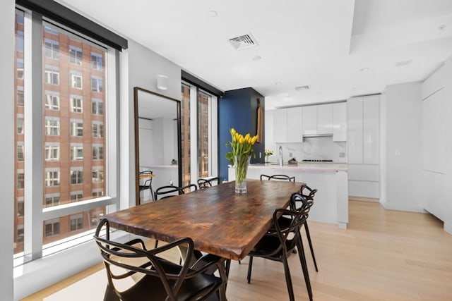 dining space with expansive windows, light wood-type flooring, and sink