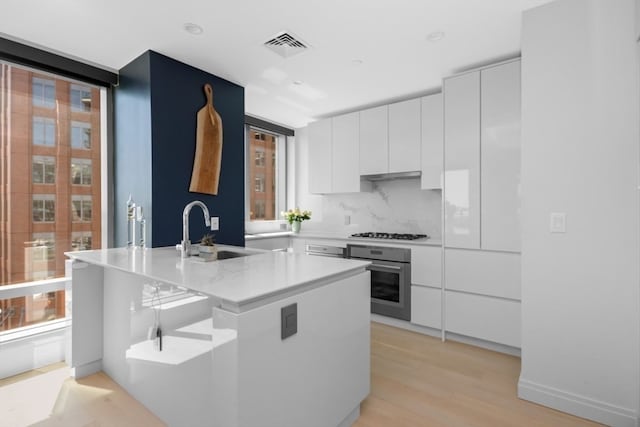 kitchen featuring white cabinetry, oven, light hardwood / wood-style floors, and sink