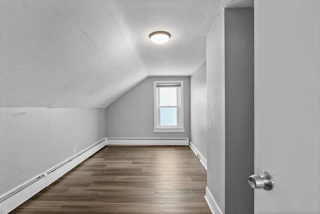 additional living space featuring dark hardwood / wood-style floors, lofted ceiling, and a baseboard heating unit