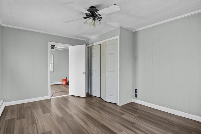 unfurnished bedroom with ceiling fan, a baseboard heating unit, wood-type flooring, a closet, and ornamental molding