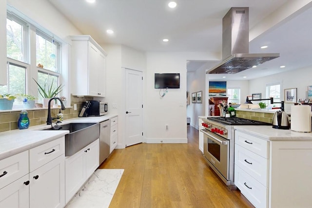 12 Lester Ter, Somerville, MA 02144 - kitchen with appliances with stainless steel finishes, island range hood, a sink, tasteful backsplash, and light wood-type flooring