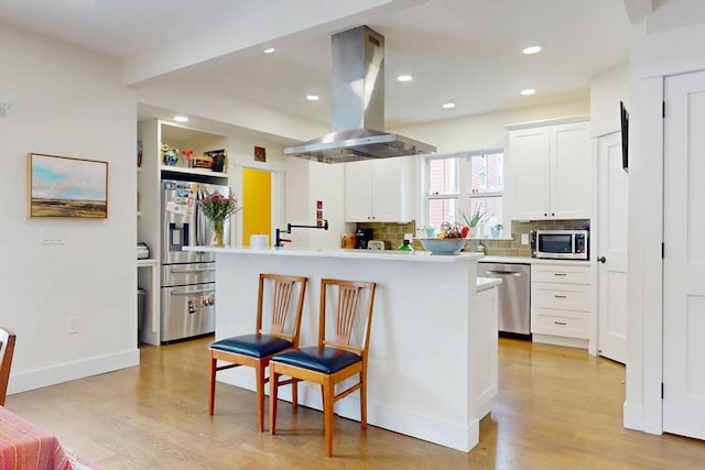 12 Lester Ter, Somerville, MA 02144 - kitchen featuring island range hood, appliances with stainless steel finishes, light wood-style flooring, decorative backsplash, and recessed lighting