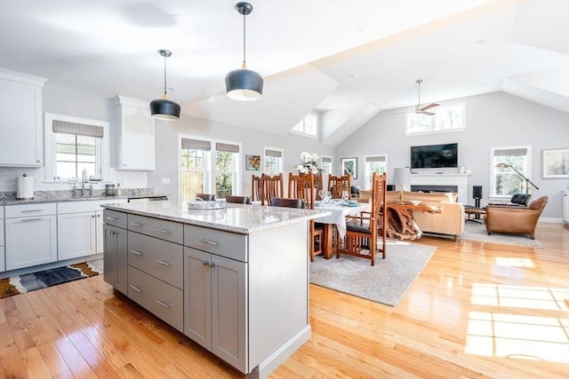 kitchen featuring light wood finished floors, a center island, gray cabinetry, a fireplace, and a sink