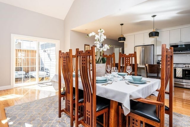 dining area with vaulted ceiling, light wood finished floors, and baseboards