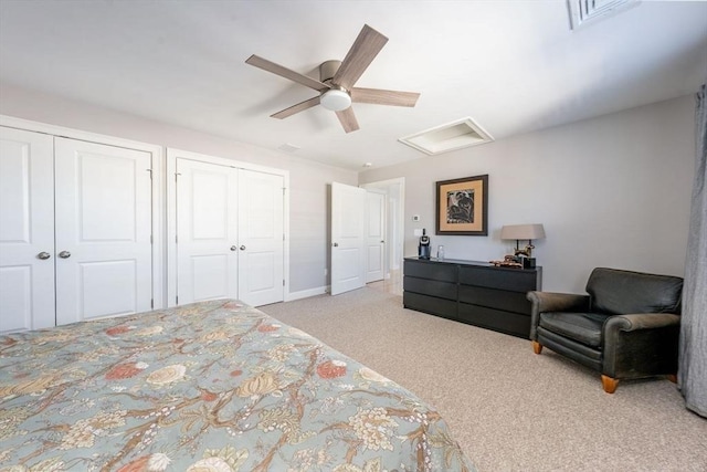 carpeted bedroom featuring attic access, visible vents, ceiling fan, and two closets