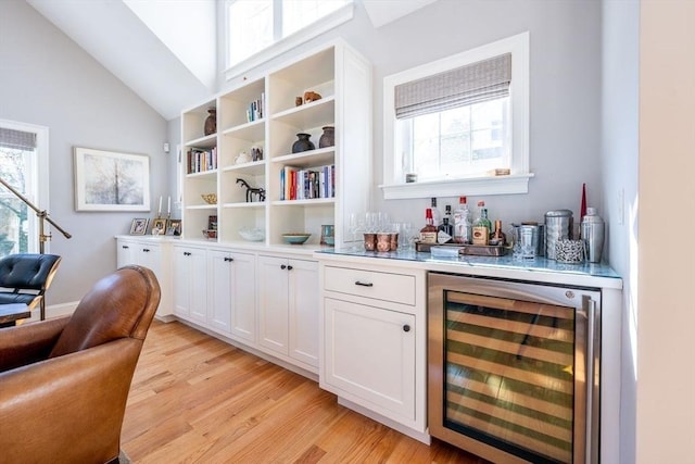 bar featuring lofted ceiling, beverage cooler, light wood finished floors, and a bar