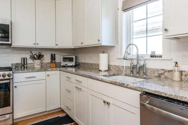 kitchen featuring light stone counters, stainless steel appliances, decorative backsplash, white cabinets, and a sink