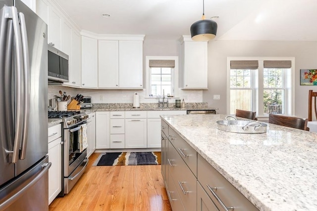 kitchen with light stone counters, appliances with stainless steel finishes, white cabinetry, and light wood-style floors