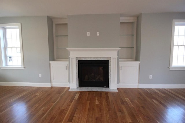 unfurnished living room featuring wood-type flooring, built in features, and a premium fireplace