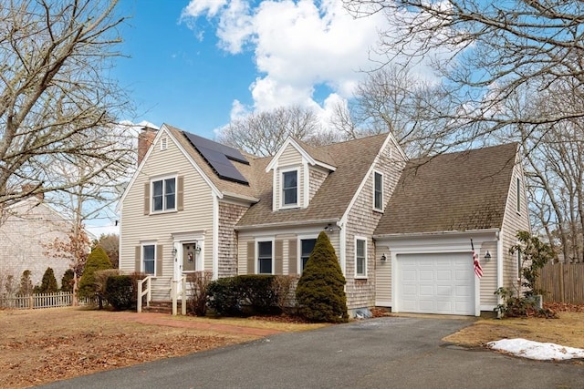 view of front facade featuring a shingled roof, roof mounted solar panels, fence, and an attached garage