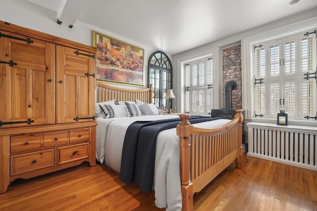 bedroom with beam ceiling, radiator heating unit, and light hardwood / wood-style floors