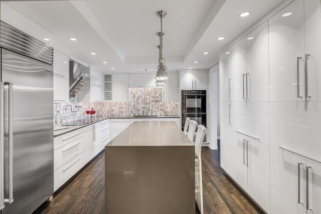 kitchen featuring a center island, hanging light fixtures, black appliances, a tray ceiling, and white cabinetry