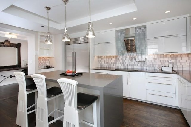 kitchen with white cabinets, built in refrigerator, and a tray ceiling