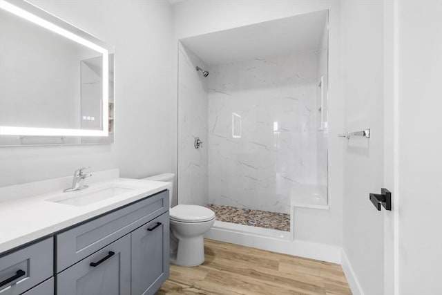 bathroom featuring hardwood / wood-style flooring, vanity, toilet, and tiled shower