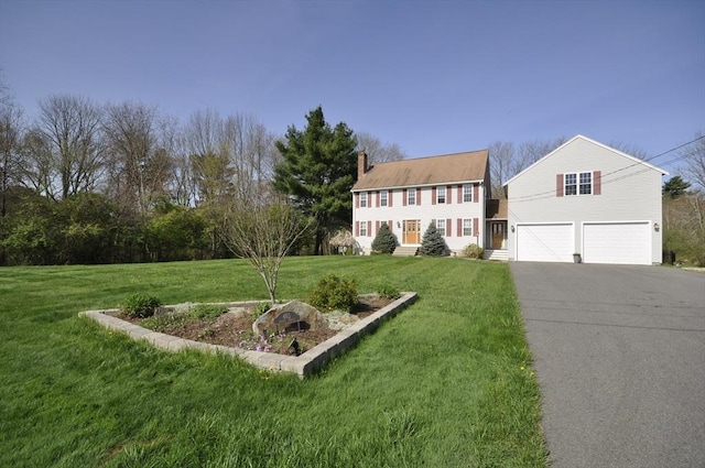 colonial-style house with a garage, a chimney, a front yard, and aphalt driveway