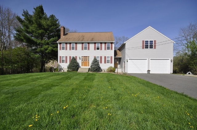 colonial home with a garage, a front yard, driveway, and a chimney