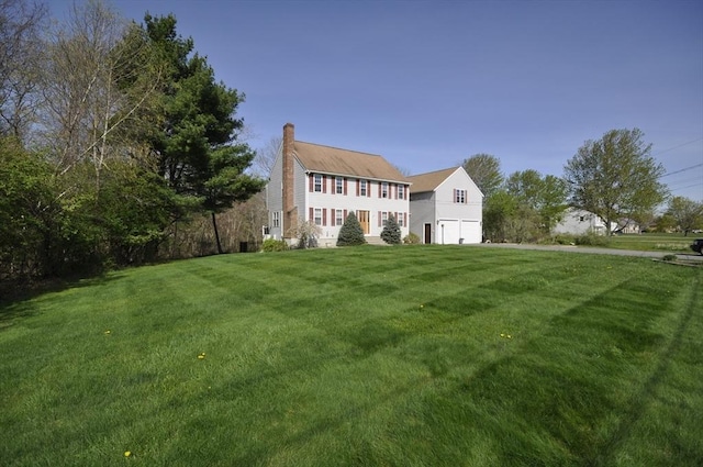back of house featuring a lawn, an attached garage, and a chimney