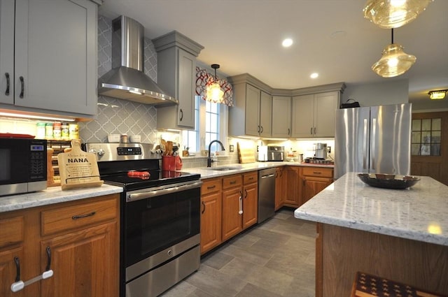 kitchen featuring wall chimney range hood, backsplash, appliances with stainless steel finishes, light stone countertops, and a sink