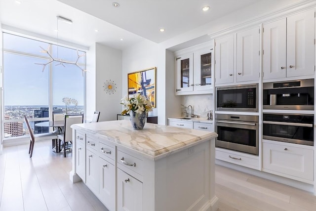kitchen with built in microwave, light wood-style flooring, a center island, a sink, and white cabinets