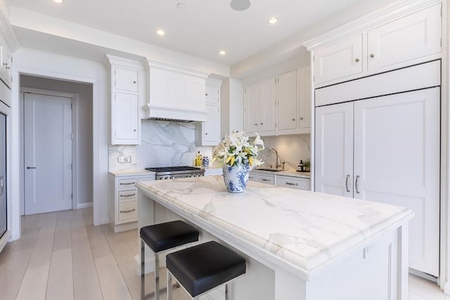 kitchen with white cabinetry, recessed lighting, backsplash, a sink, and custom range hood