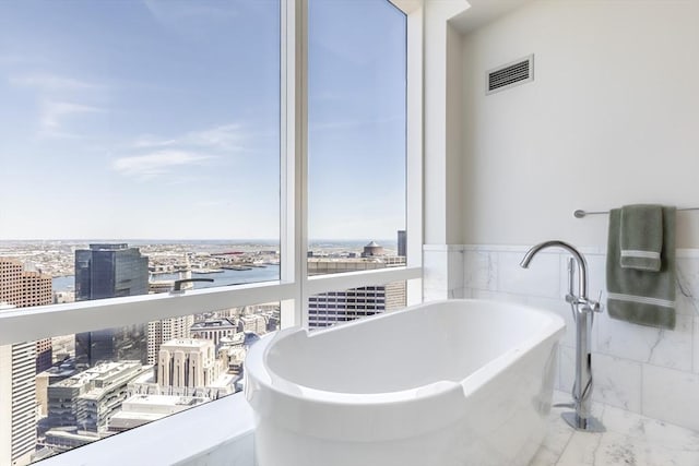 full bath with marble look tile flooring, a city view, a soaking tub, wainscoting, and tile walls