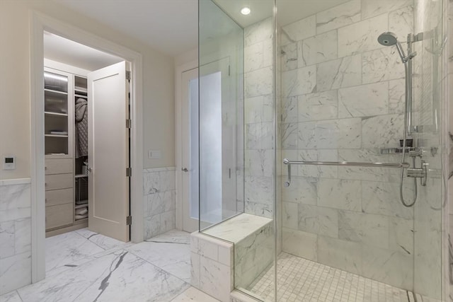 full bathroom featuring a shower stall, marble finish flooring, a spacious closet, wainscoting, and tile walls