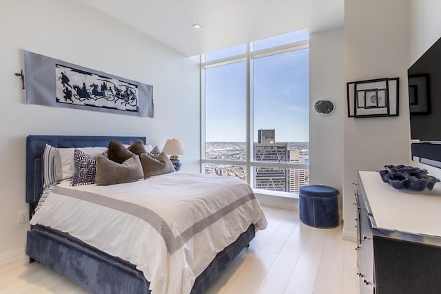 bedroom with floor to ceiling windows, light wood-type flooring, and baseboards