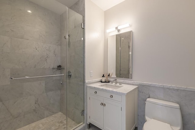 bathroom with a shower stall, toilet, vanity, and a wainscoted wall