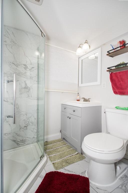 bathroom featuring a shower with door, vanity, and toilet