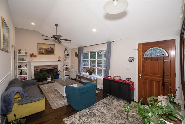 living room featuring vaulted ceiling, a brick fireplace, dark wood-type flooring, and ceiling fan