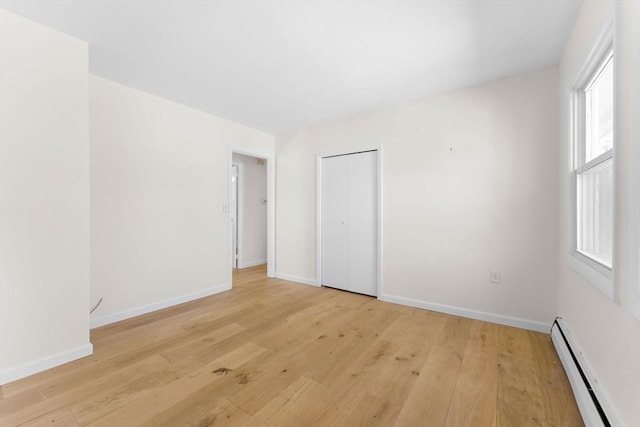 unfurnished bedroom featuring light wood-style floors, baseboards, a closet, and a baseboard radiator