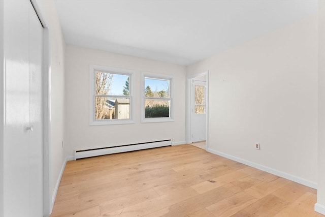 empty room featuring baseboards, a baseboard heating unit, and light wood-style floors