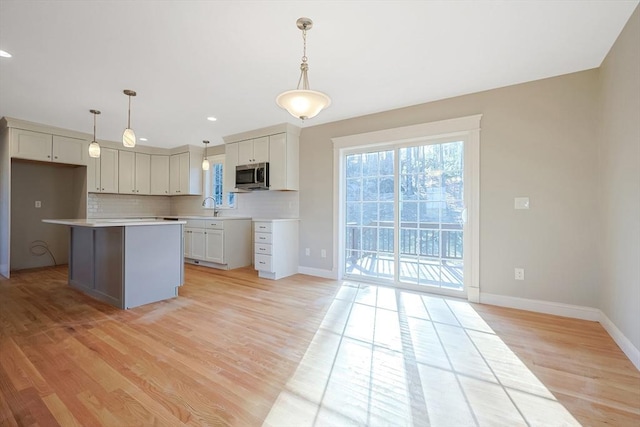 kitchen with sink, tasteful backsplash, light hardwood / wood-style floors, decorative light fixtures, and a kitchen island