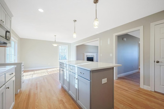 kitchen with gray cabinets, decorative light fixtures, a kitchen island, and light wood-type flooring