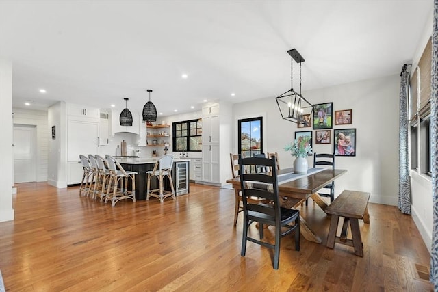 dining area with wine cooler, a notable chandelier, and light hardwood / wood-style flooring