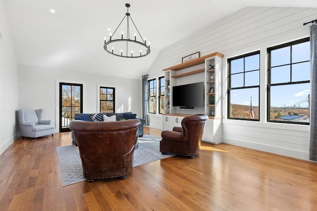 living room with vaulted ceiling, wooden walls, a chandelier, and light hardwood / wood-style flooring