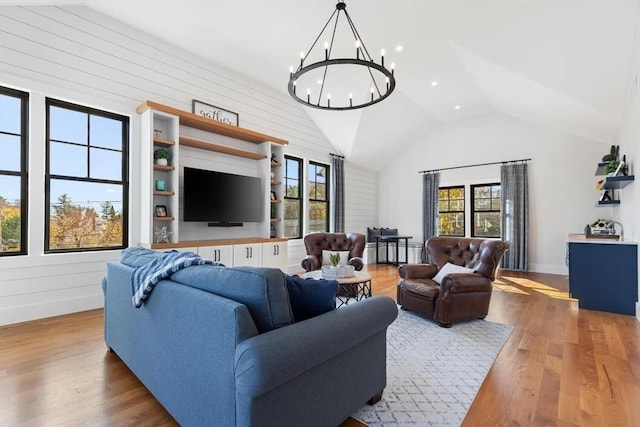 living room featuring lofted ceiling, light wood-type flooring, a notable chandelier, and wood walls