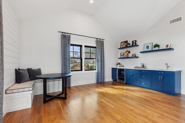 bar featuring blue cabinetry, beverage cooler, light wood-type flooring, and vaulted ceiling