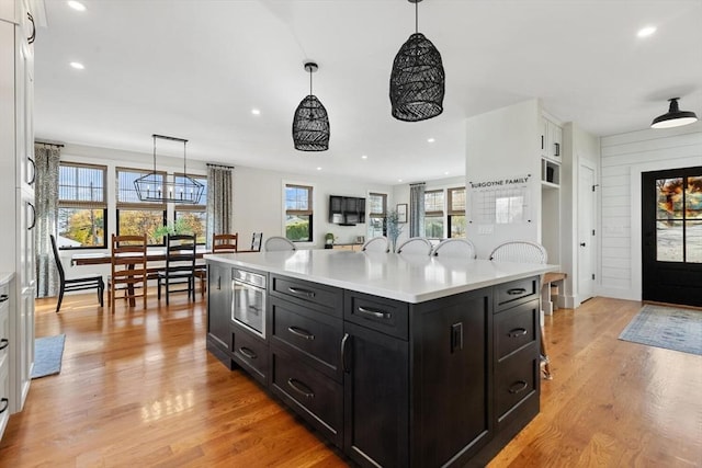 kitchen with stainless steel microwave, white cabinets, a wealth of natural light, and a center island with sink