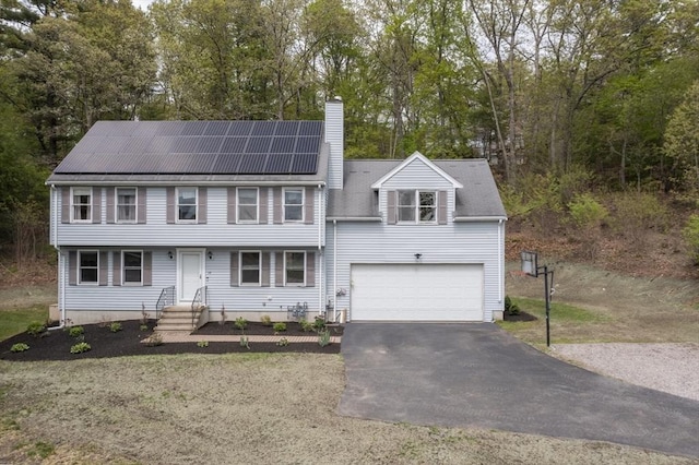 18 Candlewood Dr, Medway, MA 02053 - colonial-style house with asphalt driveway, a chimney, roof mounted solar panels, and view of scattered trees