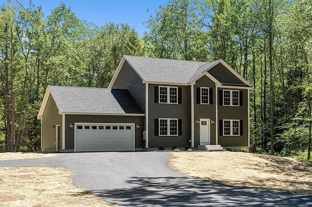 colonial-style house featuring aphalt driveway, roof with shingles, and a garage