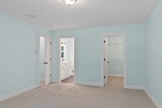 unfurnished bedroom featuring baseboards, carpet flooring, visible vents, and a walk in closet